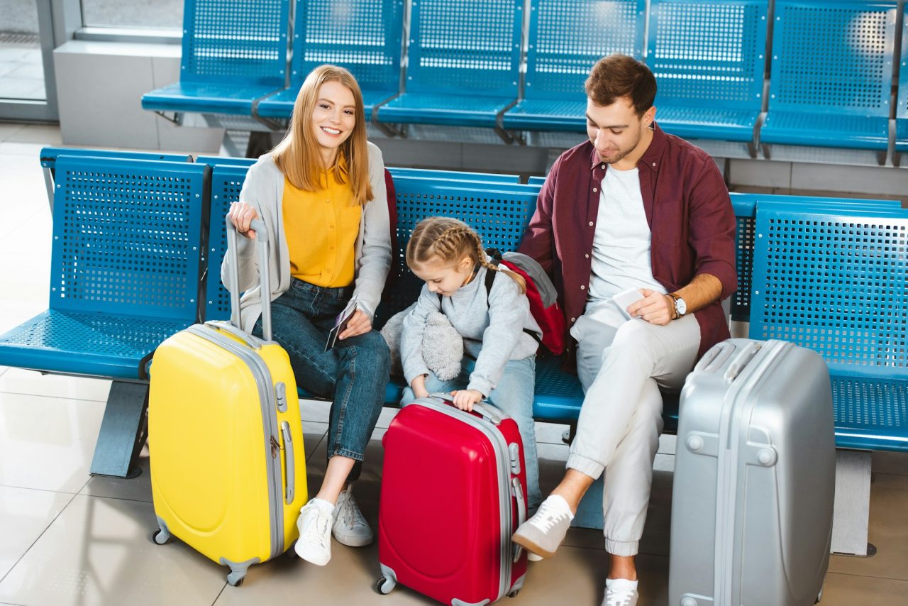 happy family sitting near luggage and smiling while waiting for flight in airport
