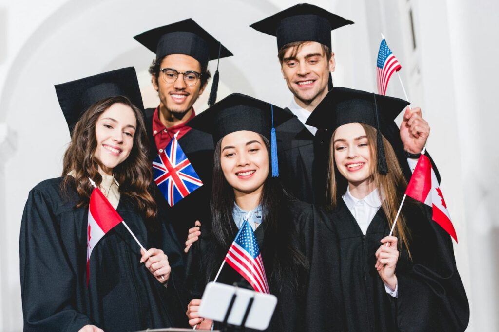 selective focus of cheerful students in graduation gowns holding flags of different countries and