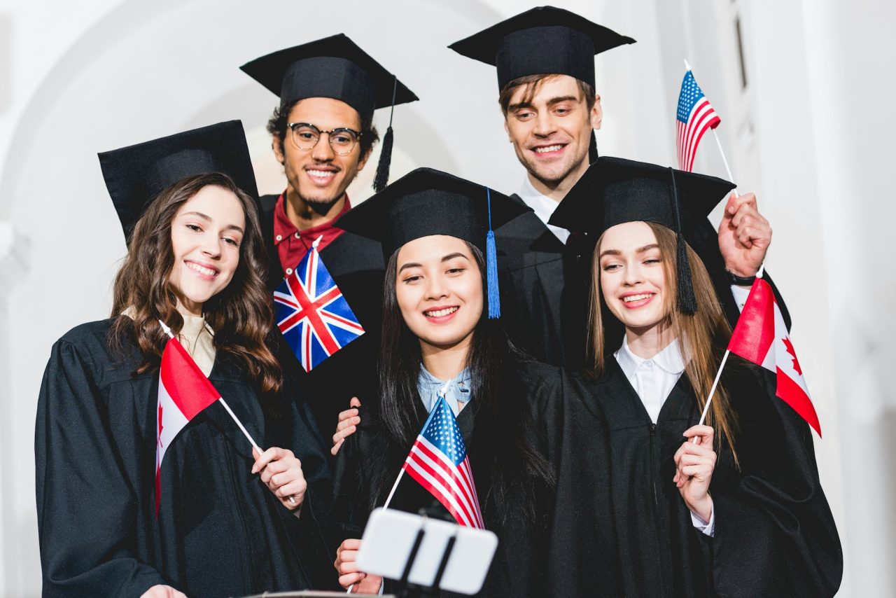 selective focus of cheerful students in graduation gowns holding flags of different countries and